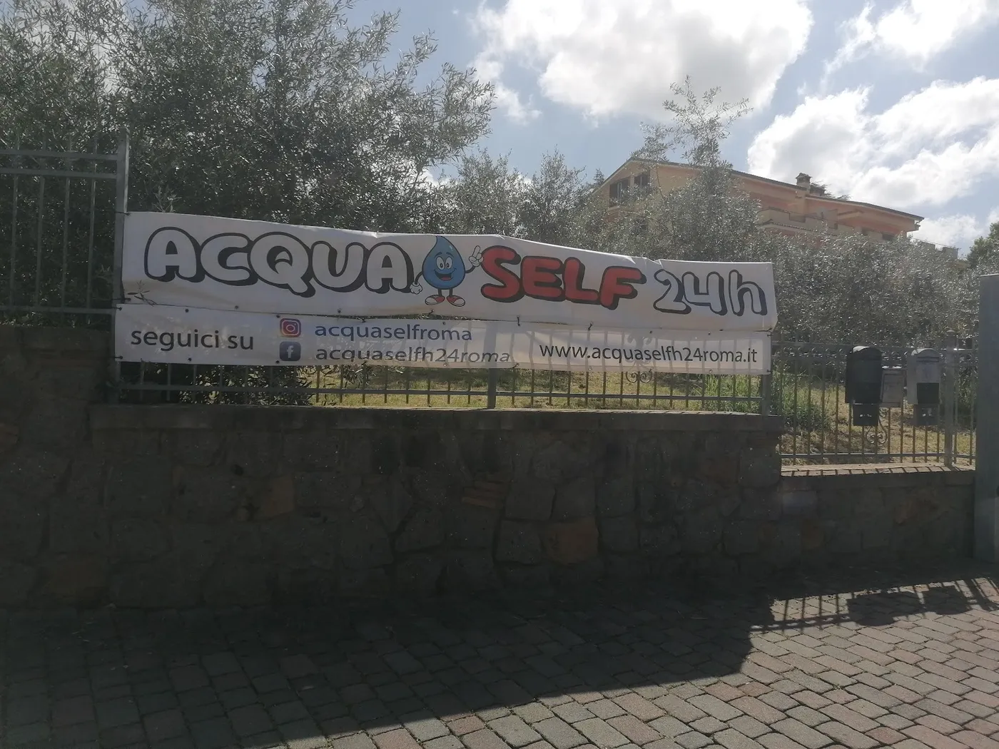 Lo striscione del distributore automatico di casse d'acqua aperto 24 ore lungo la Via Nettunense a Pavona.